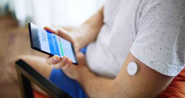 A man looking at a smartphone app to monitor his glucose levels while wearing amsart patch